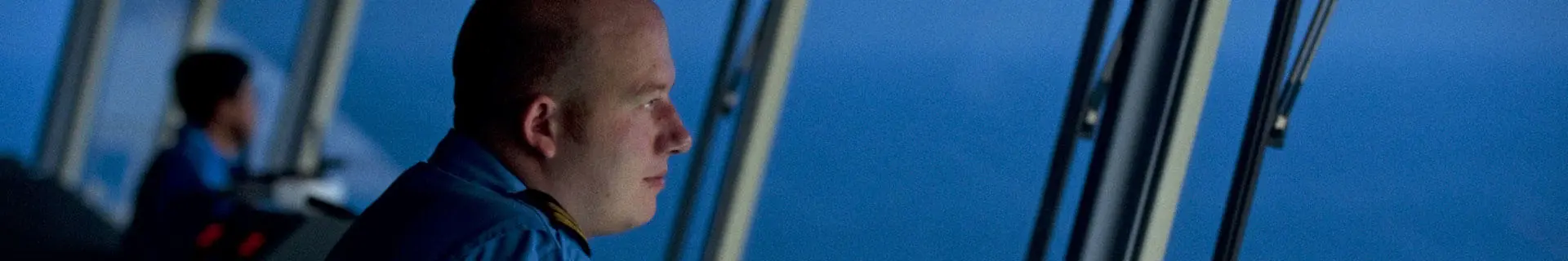 A ship's officer looking out of the window of the bridge of a ship.
