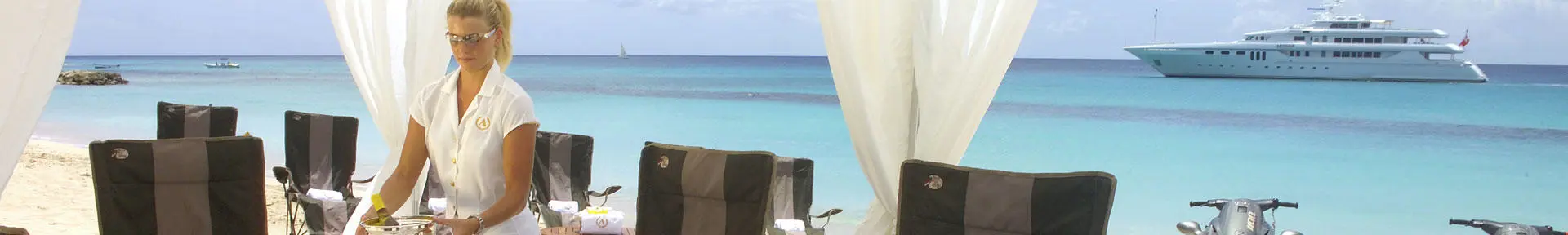 A superyacht stewardess laying a table on the beach with a superyacht in the background