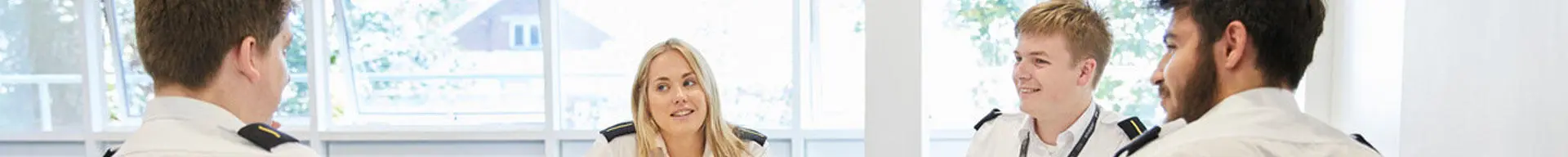 A group of deck officer cadets sat around a table with a laptop having a discussion