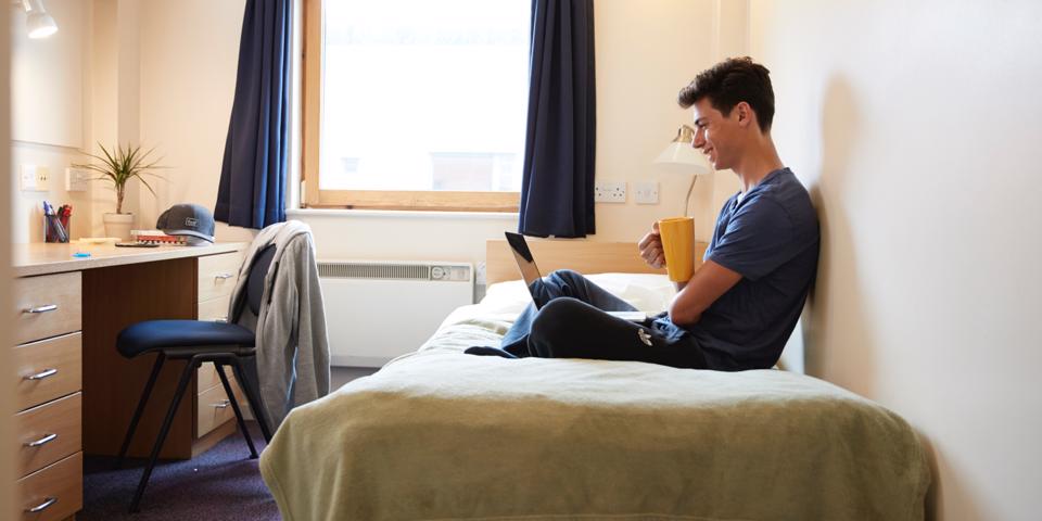 Student with a laptop sat in halls of residence room