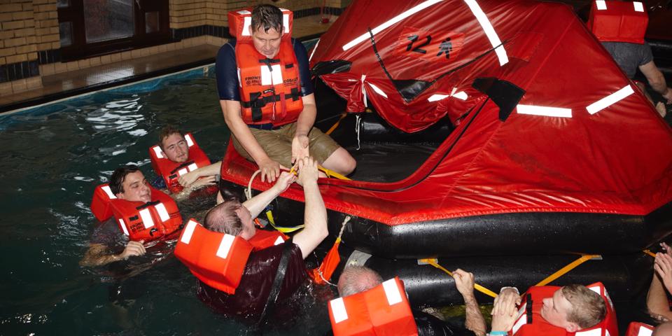 Trainees in clothes with life jackets, in a pool, completing their escape safety training with an instructor
