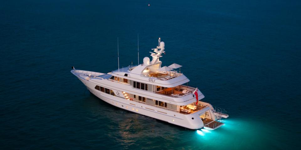 A superyacht moored up at night with lights reflecting on the sea
