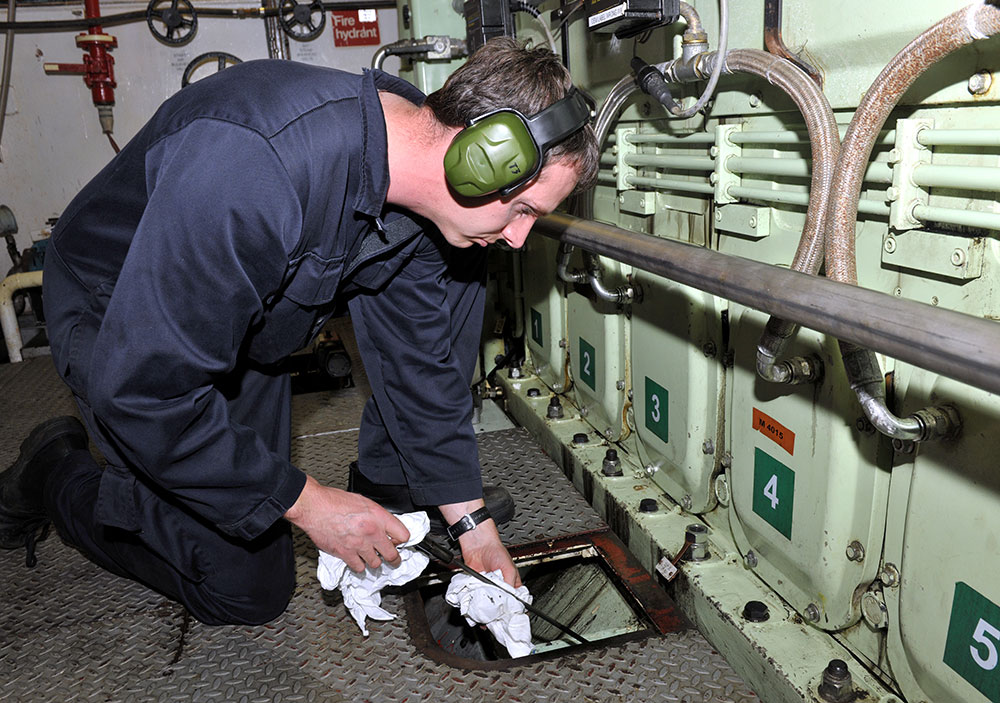 An engineer officer checking oil levels in a ship's engine room