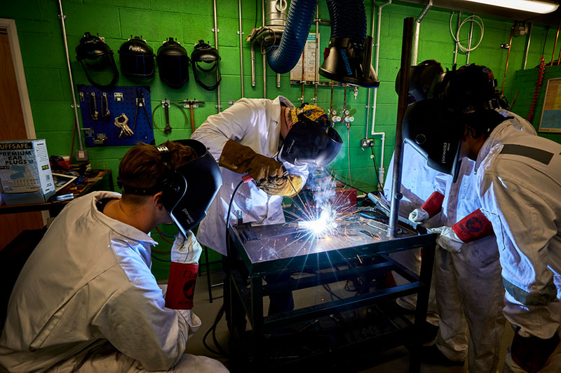 Officer cadets watching a technician demonstrating welding in the engineering workshop